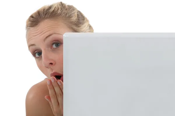 Verrast vrouw peering out achter haar laptop — Stockfoto