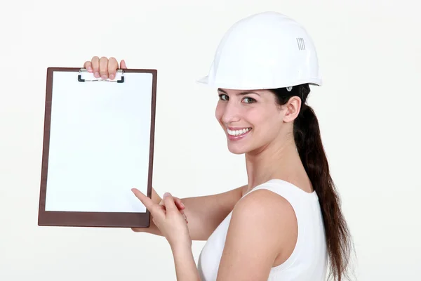 Cute female apprentice pointing at clipboard — Stock Photo, Image