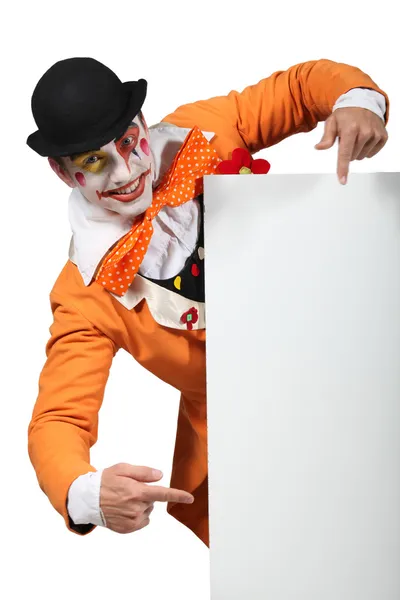 Hombre vestido como un bromista apuntando a un tablero dejado en blanco para su imagen — Foto de Stock