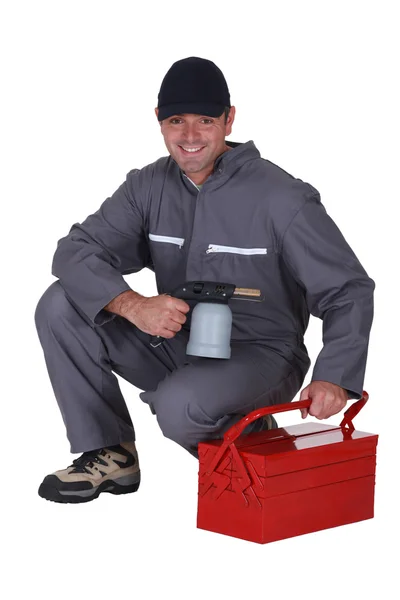 Man with blow-torch kneeling by tool kit — Stock Photo, Image