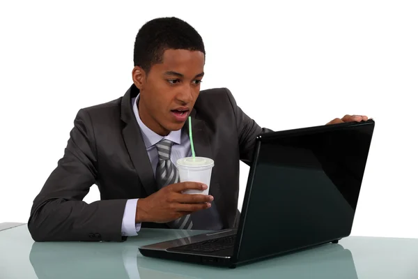 Jovem empresário afro-americano olhando para seu laptop e bebendo seu café — Fotografia de Stock