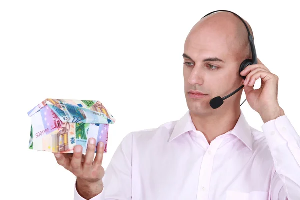 Call center agent holding a house made out of money — Stock Photo, Image