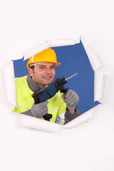 Manual worker with drill tearing through poster — Stock Photo, Image