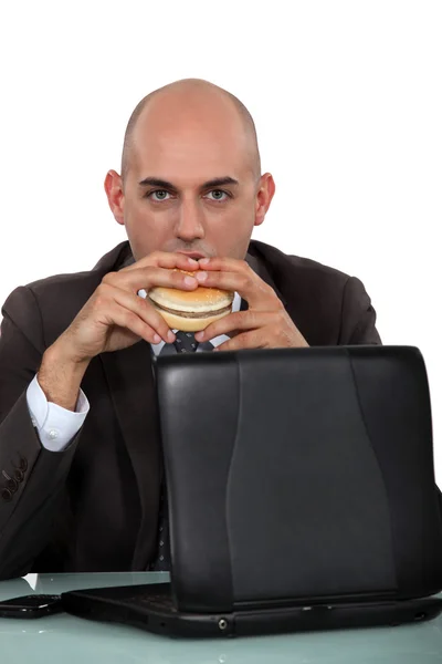 Empresário comendo um hambúrguer em sua mesa — Fotografia de Stock