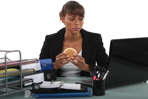 Mulher comendo um hambúrguer em sua mesa — Fotografia de Stock