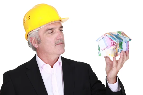 Šedá vlasy architekt drží domu z bankovek — Stock fotografie