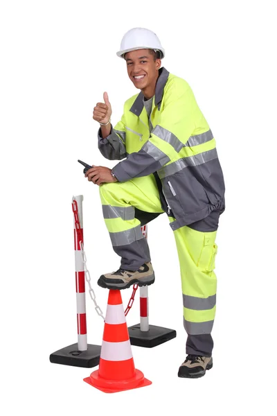 Homem em macacão de alta visibilidade com um cone de tráfego e barreira — Fotografia de Stock