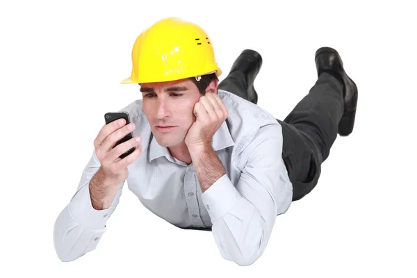 Architect lying on floor looking annoyed at sms Stock Image