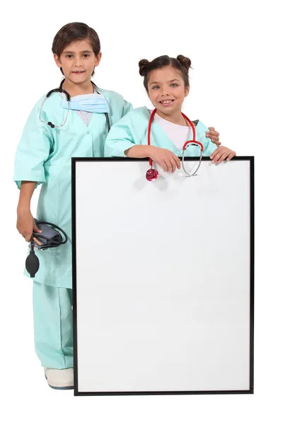 Children dressed up as doctors and standing behind a blank sign Stock Photo