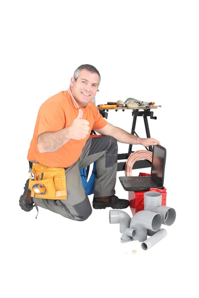 Man kneeling with laptop computer and plumbing tools Stock Image