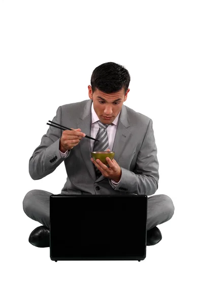 Homem comendo com pauzinhos na frente de um computador — Fotografia de Stock