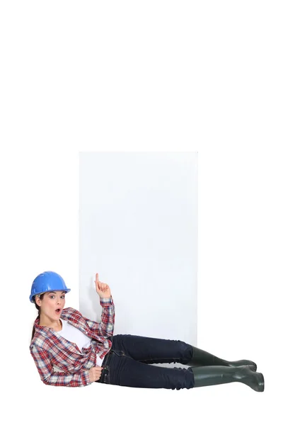 A lying female construction worker pointing at the sky. — Stock Photo, Image