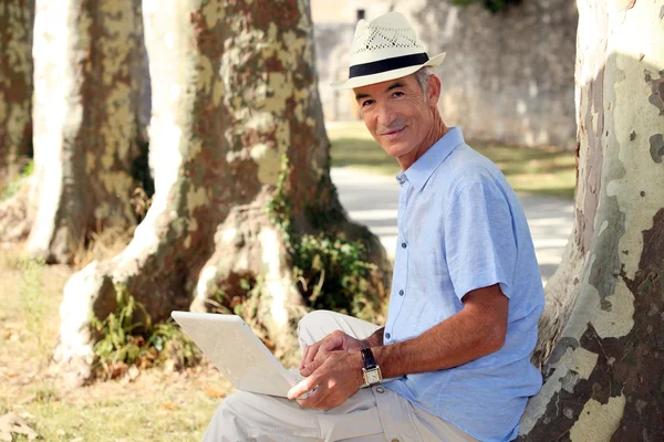 Senior man zit met een computer — Stockfoto