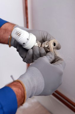Plumber wrapping flax around the joint of a pipe and thermostatic controller clipart