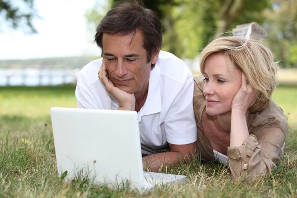 Para, leżąc na trawie patrząc na laptopa — Zdjęcie stockowe