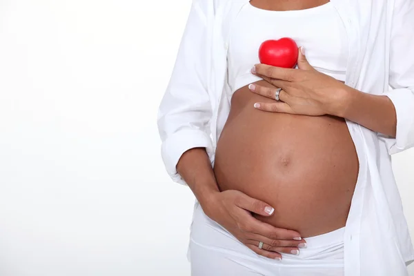 Landschaft einer schwangeren Frau, die ein Herz über ihrem entblößten Bauch hält — Stockfoto