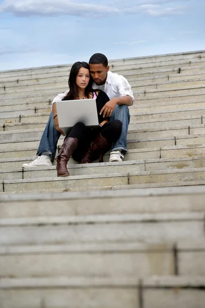 Jovem casal sentado em passos com um laptop — Fotografia de Stock