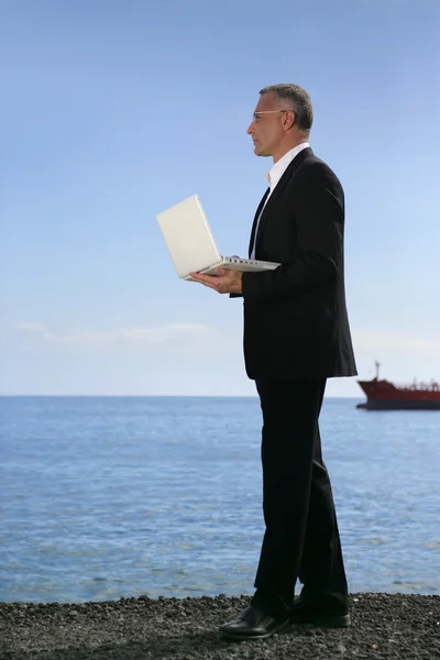 Businessman stood holding a laptop at the beach — Stock Photo, Image