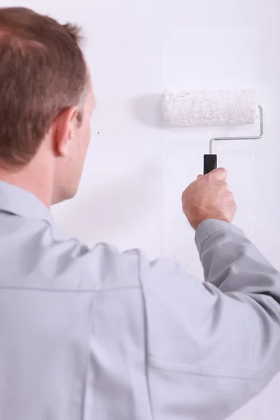 Hombre pintando una pared blanca con un rodillo — Foto de Stock