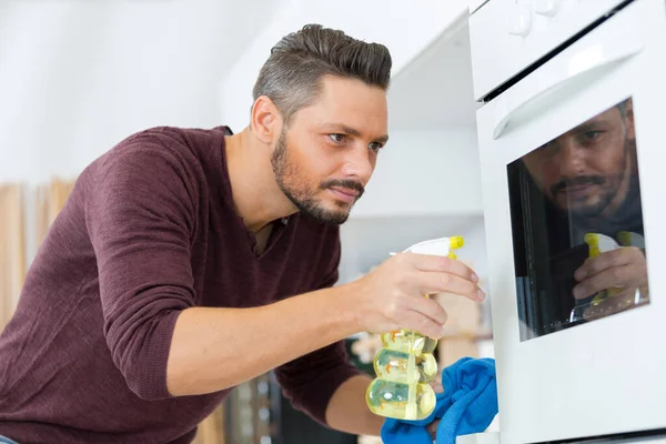 Fröhlicher Junger Hausmeister Putzt Küche Mit Spray Und Schwamm — Stockfoto