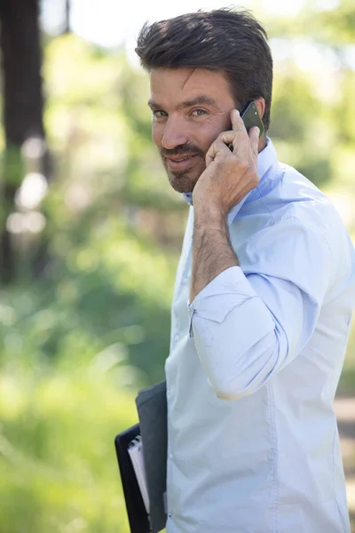 Pozytywny Przystojny Pomocą Telefonu Komórkowego Trzymając Biały Papier Ręku — Zdjęcie stockowe