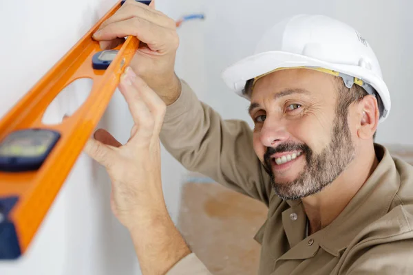 Construtor Uniforme Segurando Nível Contra Parede Dentro Casa — Fotografia de Stock