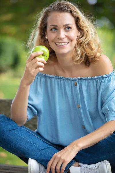 ベンチに座ってアップルを食べながら休憩する女性は — ストック写真