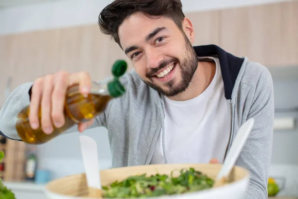 Junger Mann Gießt Olivenöl Auf Seinen Salat — Stockfoto