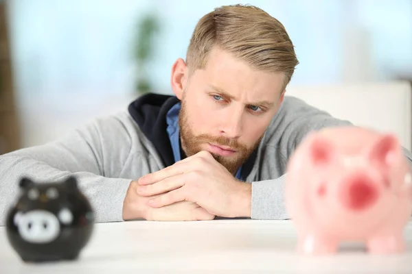 Doordachte Man Leunend Tafel Terwijl Hij Naar Piggy Bank Kijkt — Stockfoto