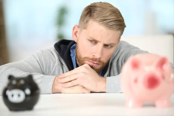 Nachdenklicher Mann Lehnt Auf Tisch Und Blickt Auf Sparschwein — Stockfoto