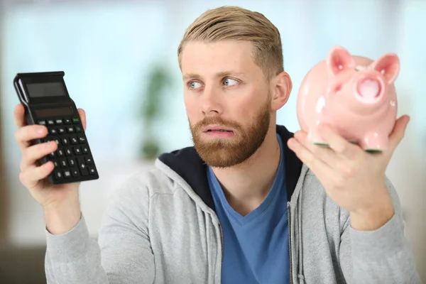 Indeciso Hombre Holding Piggybank Calculadora —  Fotos de Stock