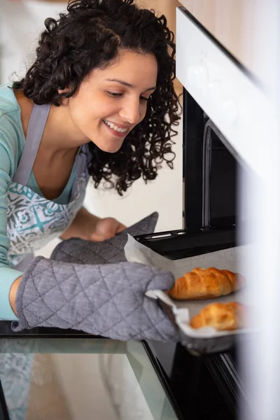 快乐的女人从烤箱里取出香甜脆的羊角面包 — 图库照片