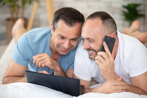 Sorrindo Gay Casal Usando Laptop Telefone Cama — Fotografia de Stock