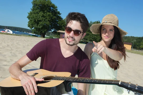 一个带着吉他和女朋友在海滩上的年轻人 — 图库照片
