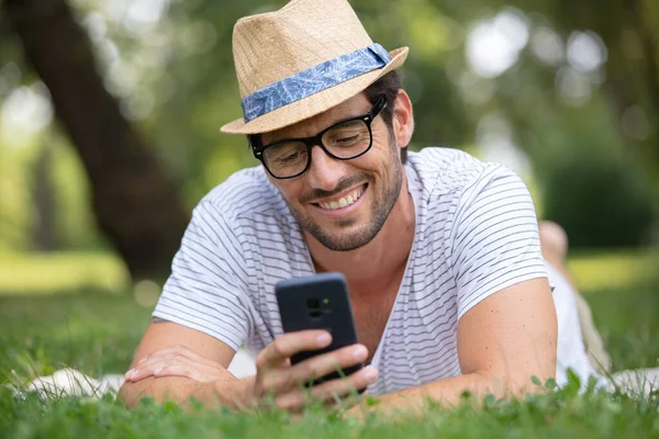 草地上英俊的男人发短信给他的约会对象 — 图库照片
