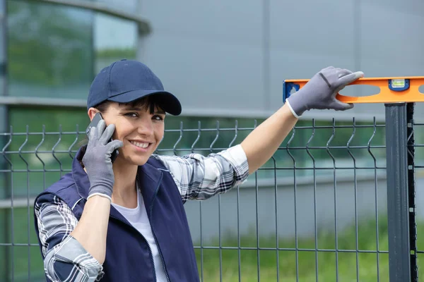 Kvinna Kontrollera Nivån Metall Staket Och Använda Telefon — Stockfoto