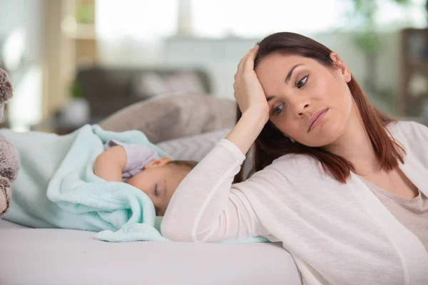 tired mother sleeping beside her sleepy daughter on a bed