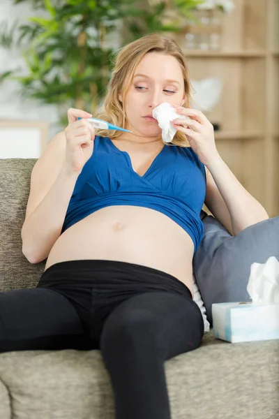 温度計付きソファに座って妊娠中の女性 — ストック写真