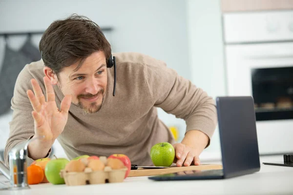 料理をしながらノートパソコンで手を振る幸せな男 — ストック写真