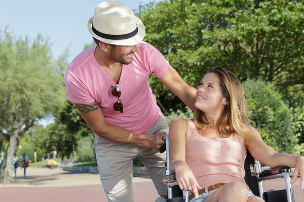 一个英俊的男人把漂亮的女人推上了公园的轮椅 — 图库照片