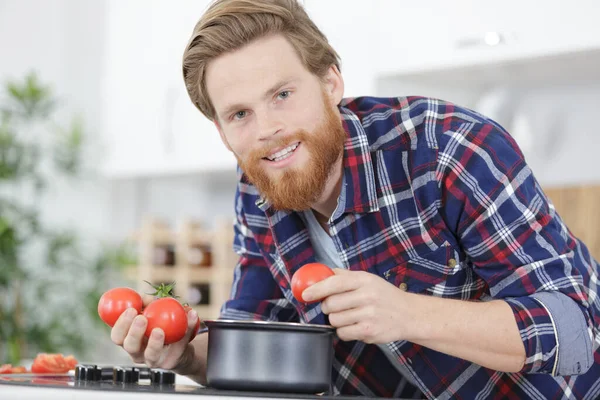 髭を生やした男が鍋の上にトマトを持ち — ストック写真