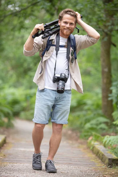 森林に対してヴィンテージフィルムの写真カメラを保持するファッショナブルなバックパッカー — ストック写真