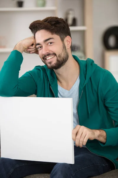 Young Man Sat Sofa Holding Blank Sign — Stock Photo, Image