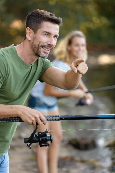 魚棒を持った男が水中を指差している — ストック写真