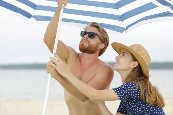 Joven Pareja Erigiendo Parasol Playa —  Fotos de Stock