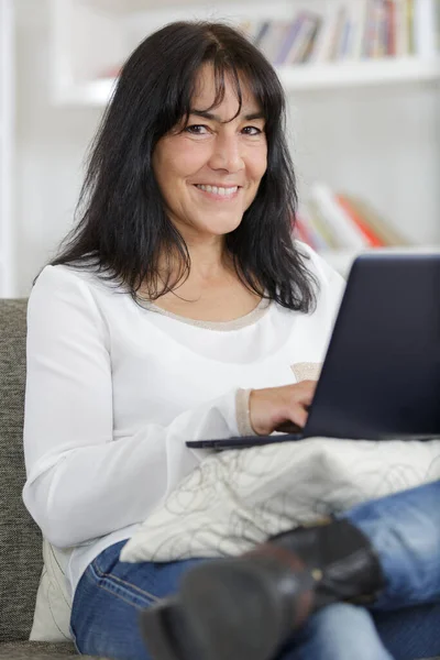 ソファの上でノートパソコンを使う中年女性 — ストック写真