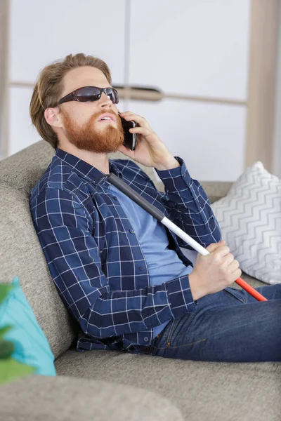 智能手机语音通话时 坐在沙发上的盲目青年 — 图库照片