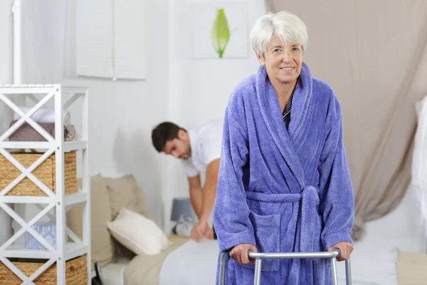 Verpleger Maken Bed Terwijl Vrouwelijke Senior Met Behulp Van Walker — Stockfoto