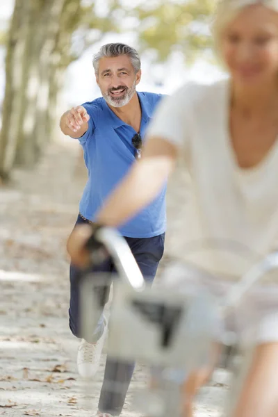 市内のサイクリング ガールフレンドを追いかけて走る先輩は — ストック写真
