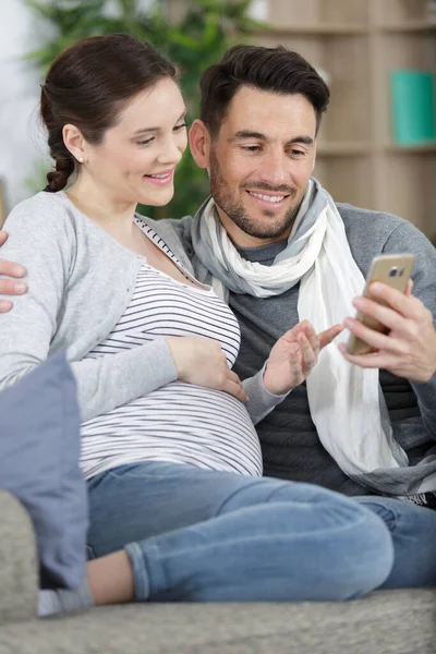 Pregnant Couple Use Smart Phone Sitting Couch — Stock Photo, Image